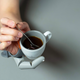 A person supporting a coffee cup with the Third Thumb, while stirring a spoon with their natural fingers.